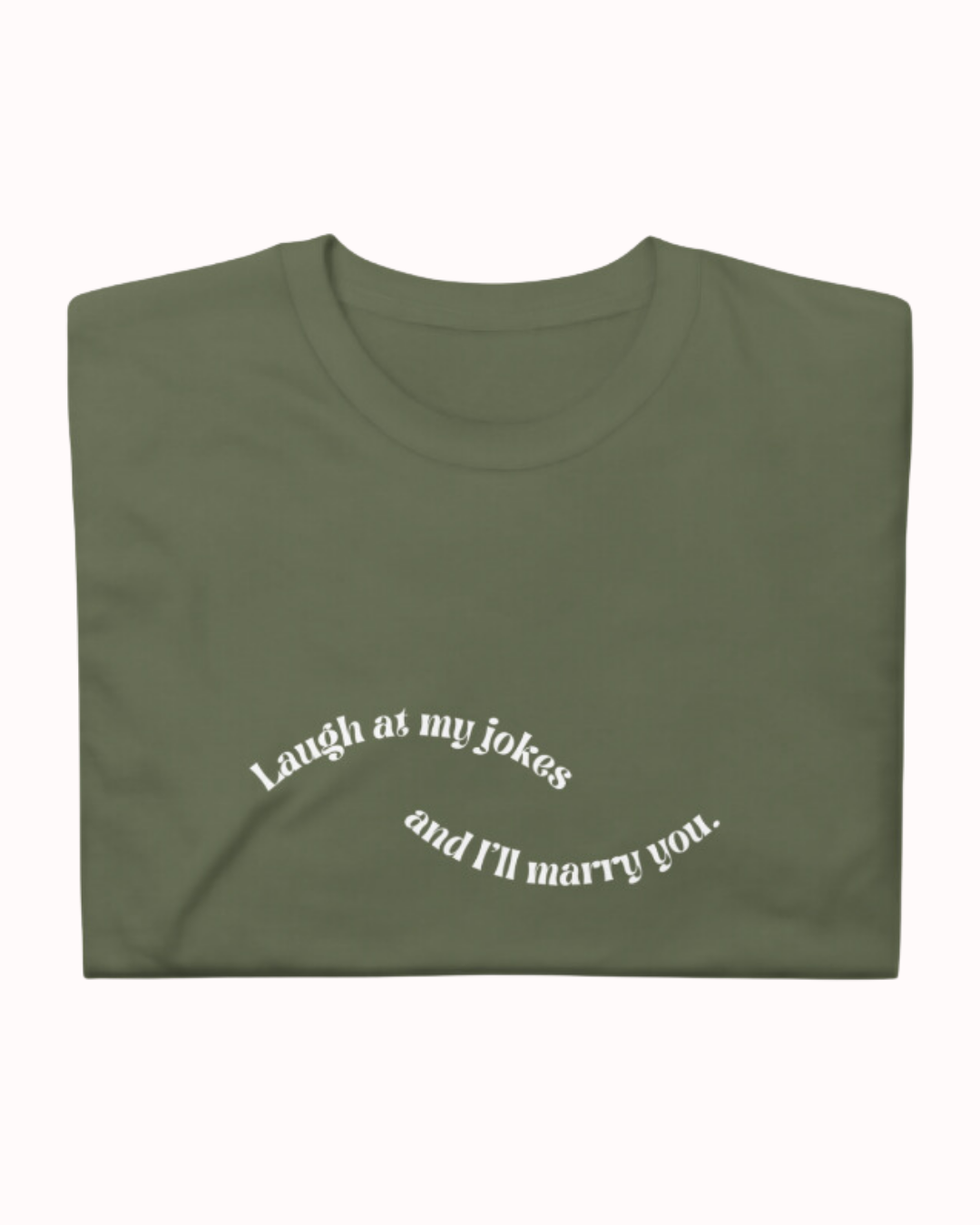 forest green T-Shirt with the phrase 'Laugh at my jokes and I will marry you' on the chest, displayed against a vibrant café-style backdrop with a pink counter and cozy decoration with plants. A playful and bold design for fans of funny merchandise and sarcasm.