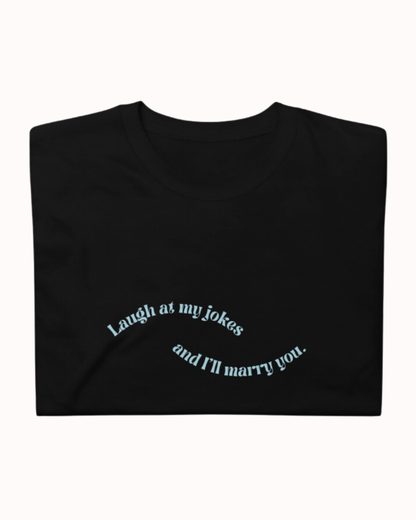 Folded black T-Shirt featuring the ironic phrase 'Laugh at my jokes and I will marry you'. Perfect for fans of funny merchandise, bold humor, and witty sarcasm. 