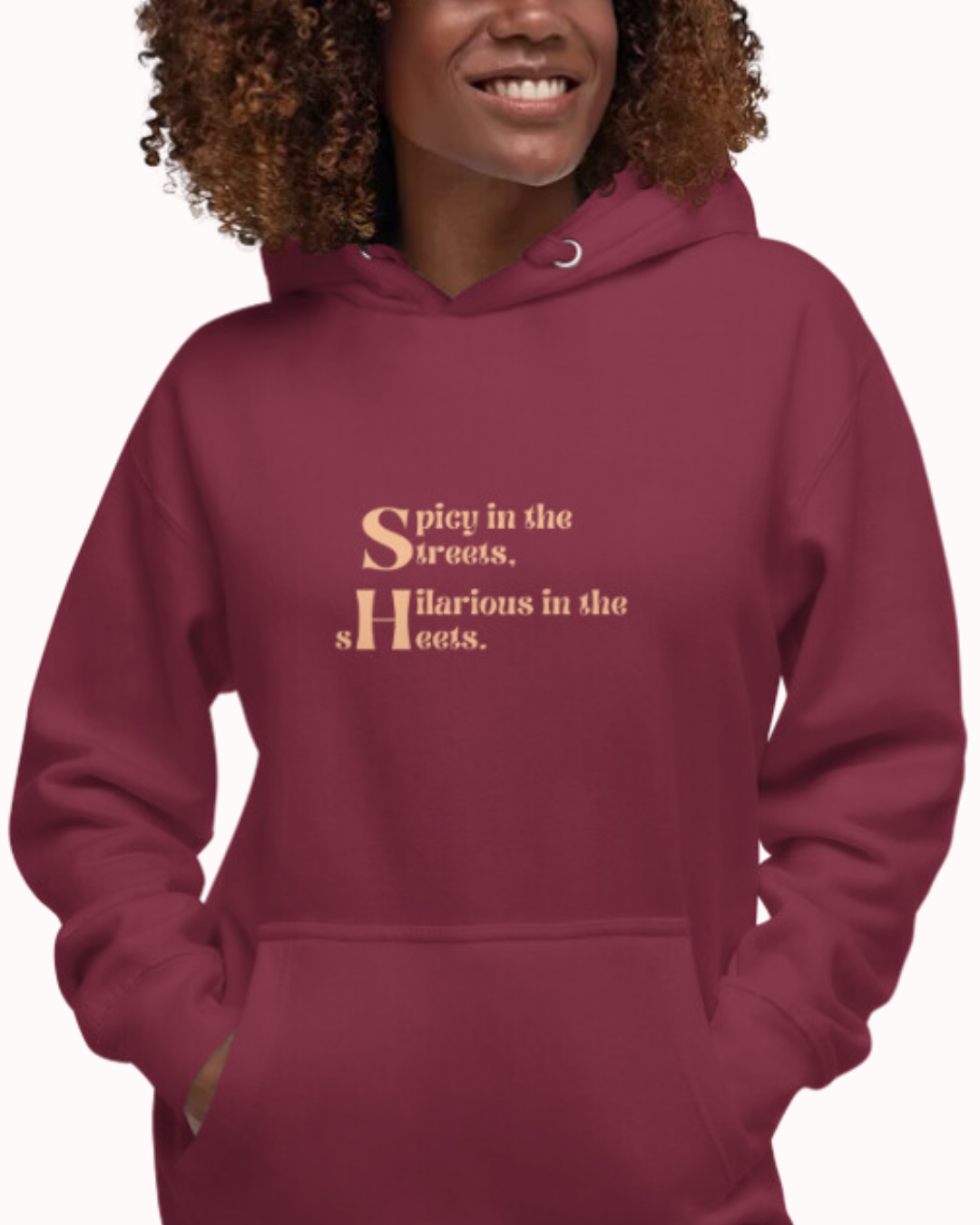 Front view of a maroon hoodie worn by a smiling woman, featuring the phrase 'Spicy in the streets, Hilarious in the sheets' on the chest. Perfect for fans of funny merchandise, bold humor, and witty sarcasm.