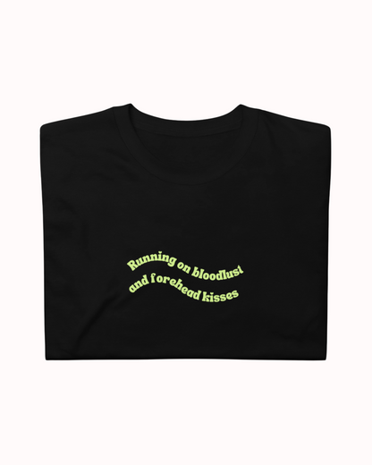 Folded Black t-shirt featuring the ironic phrase "Running on bloodlust and forehead kisses". Perfect for fans of funny merchandise, bold humor, and witty sarcasm.