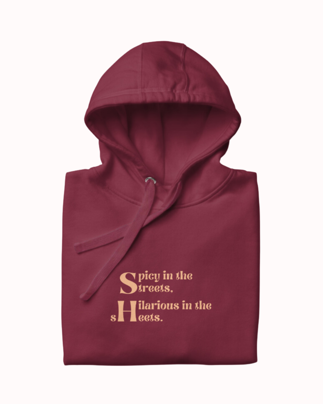 Folded maroon hoodie featuring the ironic phrase 'Spicy in the streets, Hilarious in the sheets'. Perfect for fans of funny merchandise, bold humor, and witty sarcasm. 