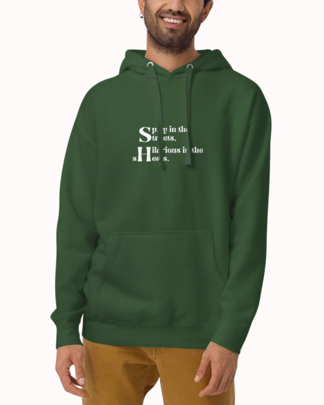 Front view of a forest green hoodie worn by a smiling man, featuring the phrase 'Spicy in the streets, Hilarious in the sheets' on the chest. Perfect for fans of funny merchandise, bold humor, and witty sarcasm.