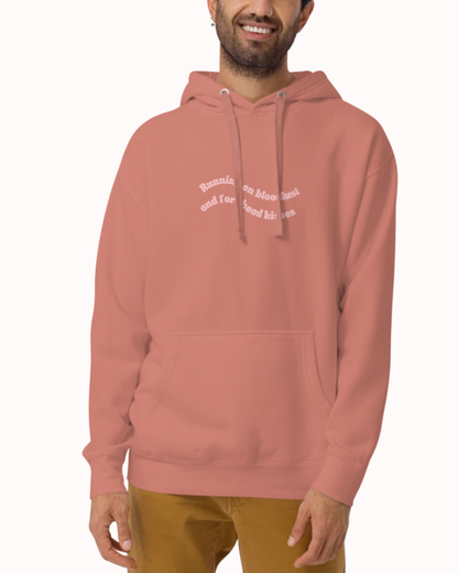 Front view of a Dusty Rose hoodie worn by a smiling man, featuring the phrase "Running on bloodlust and forehead kisses" on the chest and back. Perfect for fans of funny merchandise, bold humor, and witty sarcasm.