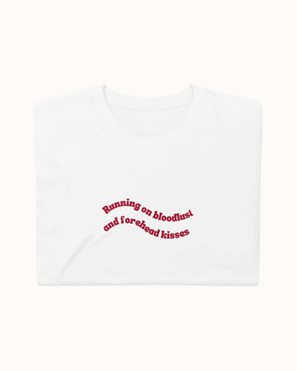 Folded White t-shirt featuring the ironic phrase "Running on bloodlust and forehead kisses". Perfect for fans of funny merchandise, bold humor, and witty sarcasm.