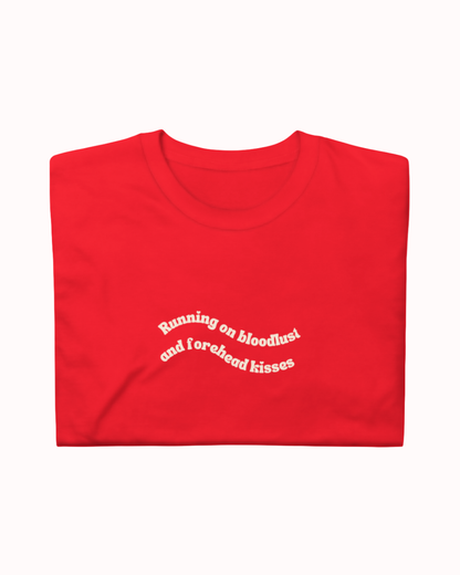 Folded Red t-shirt featuring the ironic phrase "Running on bloodlust and forehead kisses". Perfect for fans of funny merchandise, bold humor, and witty sarcasm.