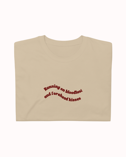 Folded Sand t-shirt featuring the ironic phrase "Running on bloodlust and forehead kisses". Perfect for fans of funny merchandise, bold humor, and witty sarcasm.