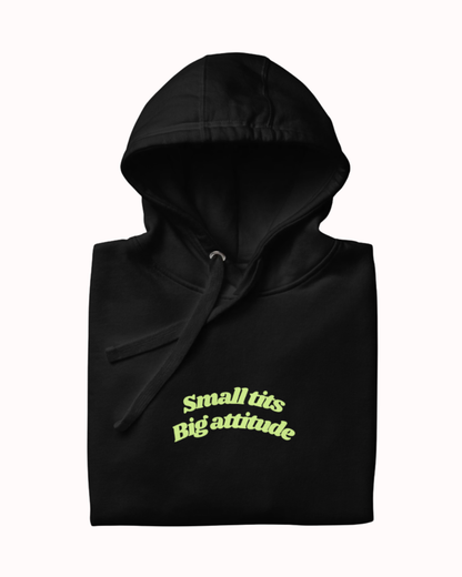 Folded Black hoodie featuring the ironic phrase "Small tits. Big attitude". Perfect for fans of funny merchandise, bold humor, and witty sarcasm.